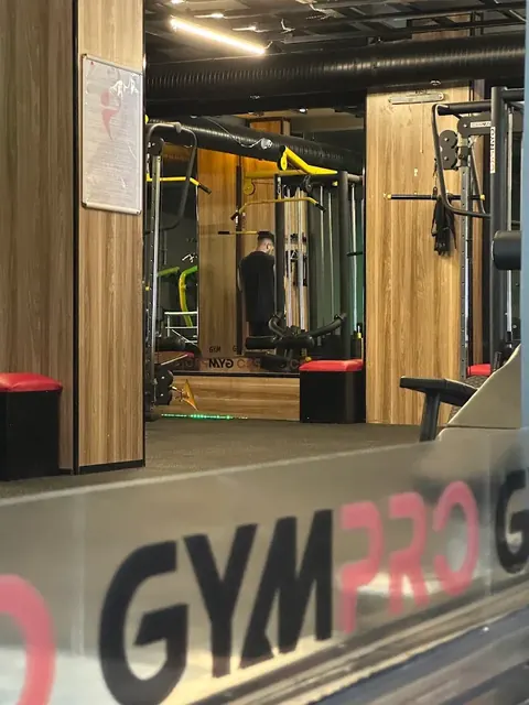 Ön planda cam üzerinde GYMPRO logosu, arkada antrenman alanı